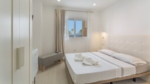 A bedroom with a bed, bedside table, bench, window, and curtains.