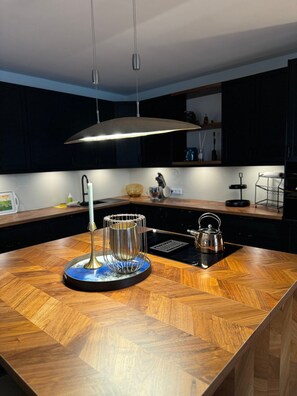 A modern kitchen with a wooden countertop, a kettle, a coffee maker, and a pendant light. - 180sqm Penthouse 2 Bedrooms incl. Terrace & Underground Parking (Rostock)