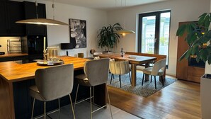 Una cocina moderna con una isla de madera, taburetes de bar, iluminación colgante y un amplio ventanal con vistas.