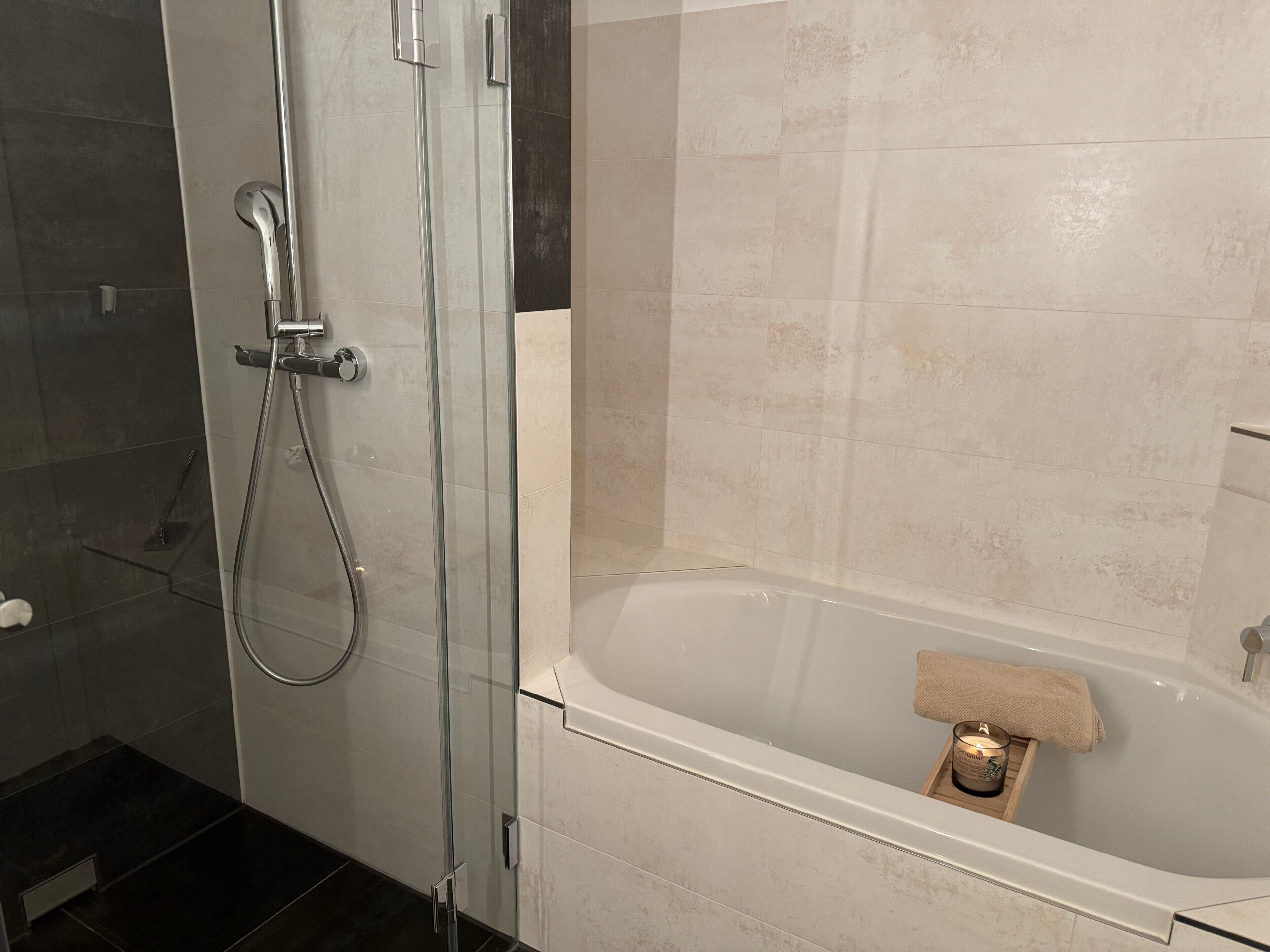 A modern bathroom with a glass-enclosed shower, a bathtub with a candle, and a towel on the edge.