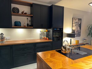 Une cuisine moderne avec des meubles de couleur noire, un plan de travail en bois, un four encastré et une machine à café.