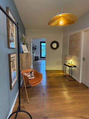 Un couloir avec un plancher en bois, une chaise, un luminaire suspendu et une porte.