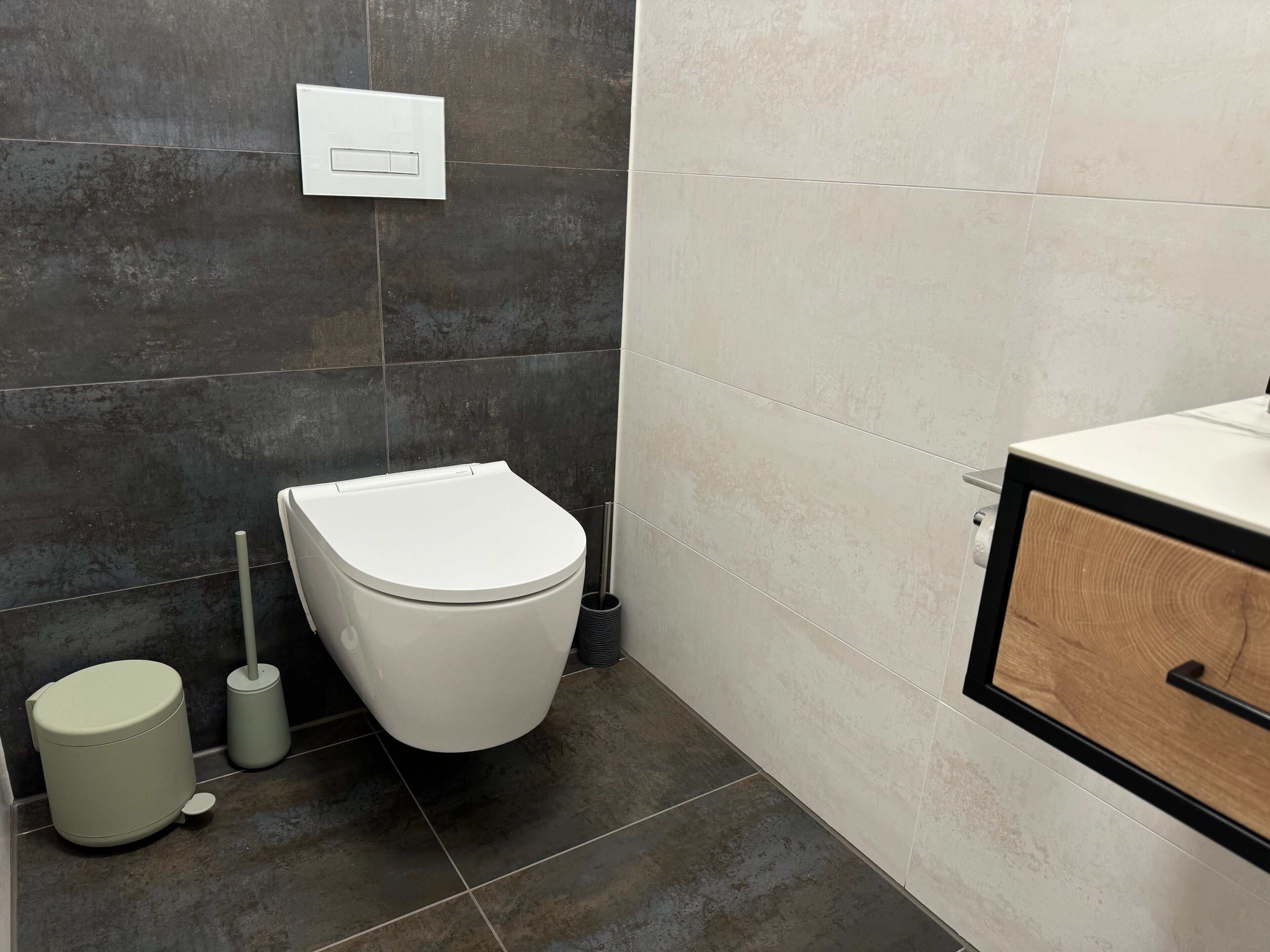 A bathroom with a toilet, a bidet, a trash bin, and a cabinet.