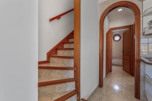 Eine Treppe mit hölzernen Geländern und beigen Marmorstufen führt zu einem Flur mit einer Holztür und einem Rundfenster.