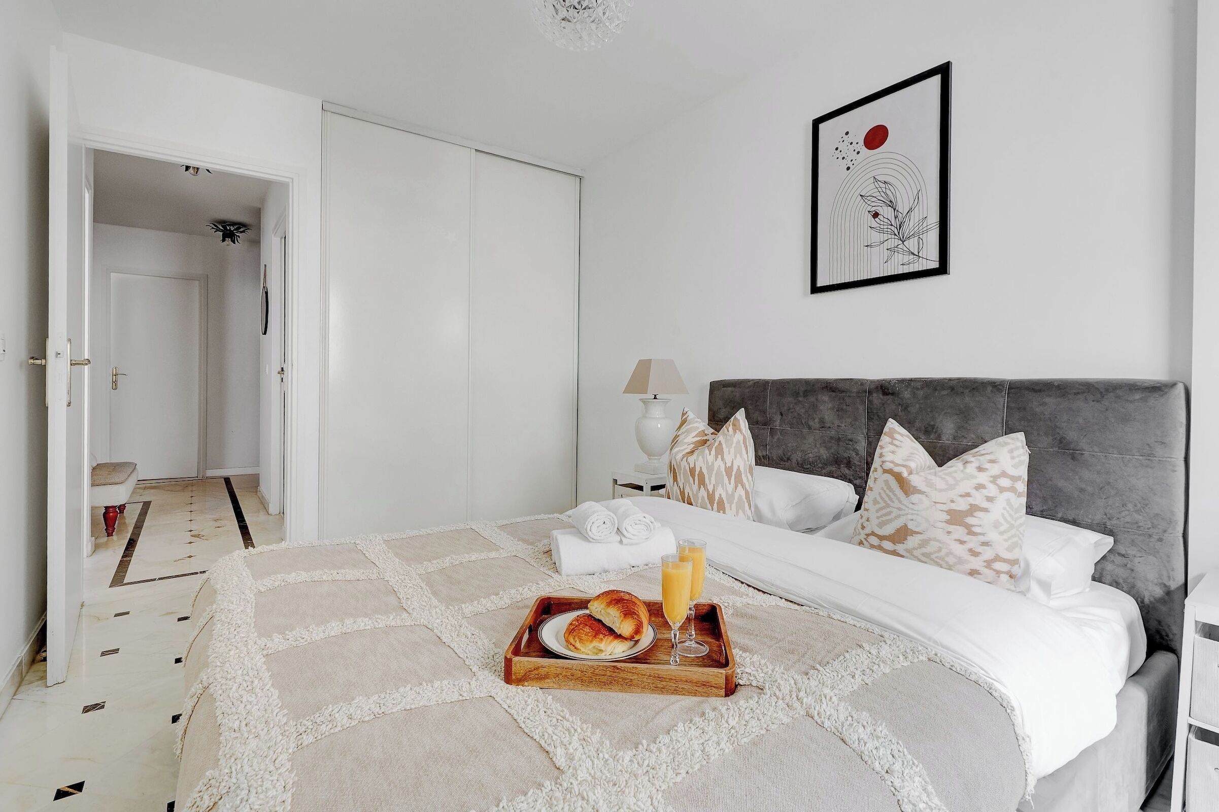 Un dormitorio ordenado con cama, mesita de noche y una bandeja con alimentos para el desayuno.
