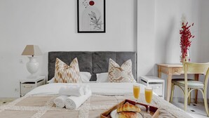 A neatly made bed with pillows, a bedside table with a lamp, a tray with croissants and juice, and a chair.
