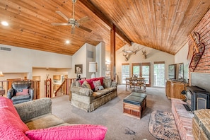 A spacious living area with a high ceiling, wooden beams, a fireplace, and a dining area with a view of the outdoors.