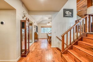 A wooden staircase leading to a second floor, a dining area with a table and chairs, and a hallway with a wooden floor and a mounted deer head.