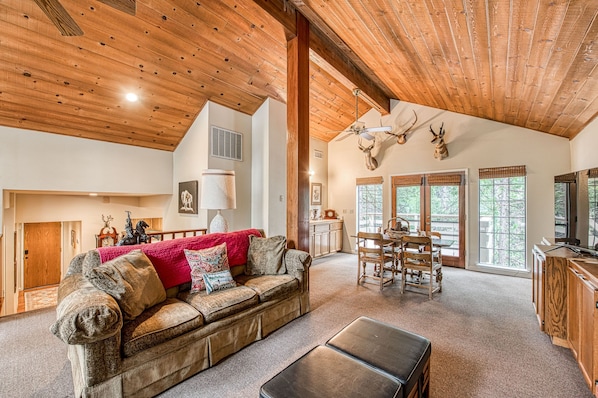 A spacious living room with a wooden ceiling, a cozy fireplace, a dining area, and a kitchen.