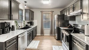 A modern kitchen with stainless steel appliances, a dishwasher, and a large window with curtains. - Backyard Oasis: Smart Home w/ Alexa & Fire Pit (Killeen)