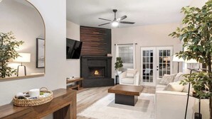 A modern living room with a fireplace, a ceiling fan, and a large mirror. - Backyard Oasis: Smart Home w/ Alexa & Fire Pit (Killeen)