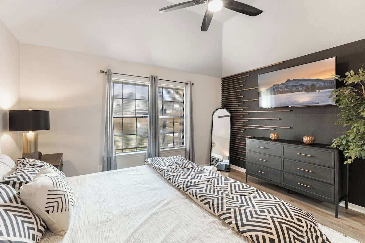 Een slaapkamer met een bed, een dressoir, een televisie en een plafondventilator.