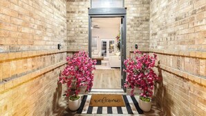 A hallway with brick walls, a welcome mat, and potted plants. - Backyard Oasis: Smart Home w/ Alexa & Fire Pit (Killeen)