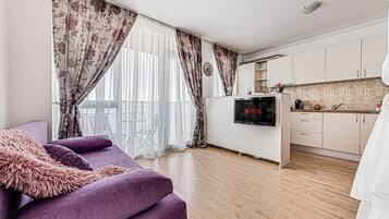 A living room with a purple sofa, a flat-screen TV, and a kitchen area with cabinets and a microwave.