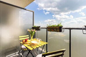 A balcony with a yellow table set for breakfast, a vase with flowers, and potted plants.