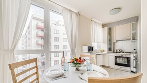 A modern kitchen with white cabinets, a microwave, and a stove. There is a dining table with chairs and a vase of flowers. - ARI - ARED Luxurious Apartments (Arad)