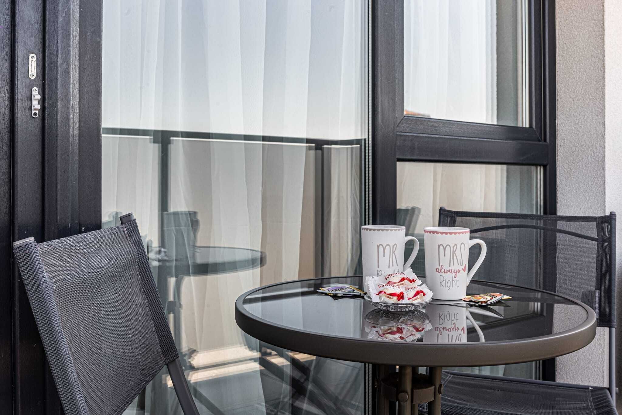 A round glass table with two mugs labeled "Mr" and "Mrs" and a small plate of cookies.