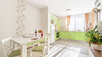 Une cuisine moderne avec des meubles de couleur verte, une table à manger blanche avec des chaises et une plante en pot posée sur le comptoir.