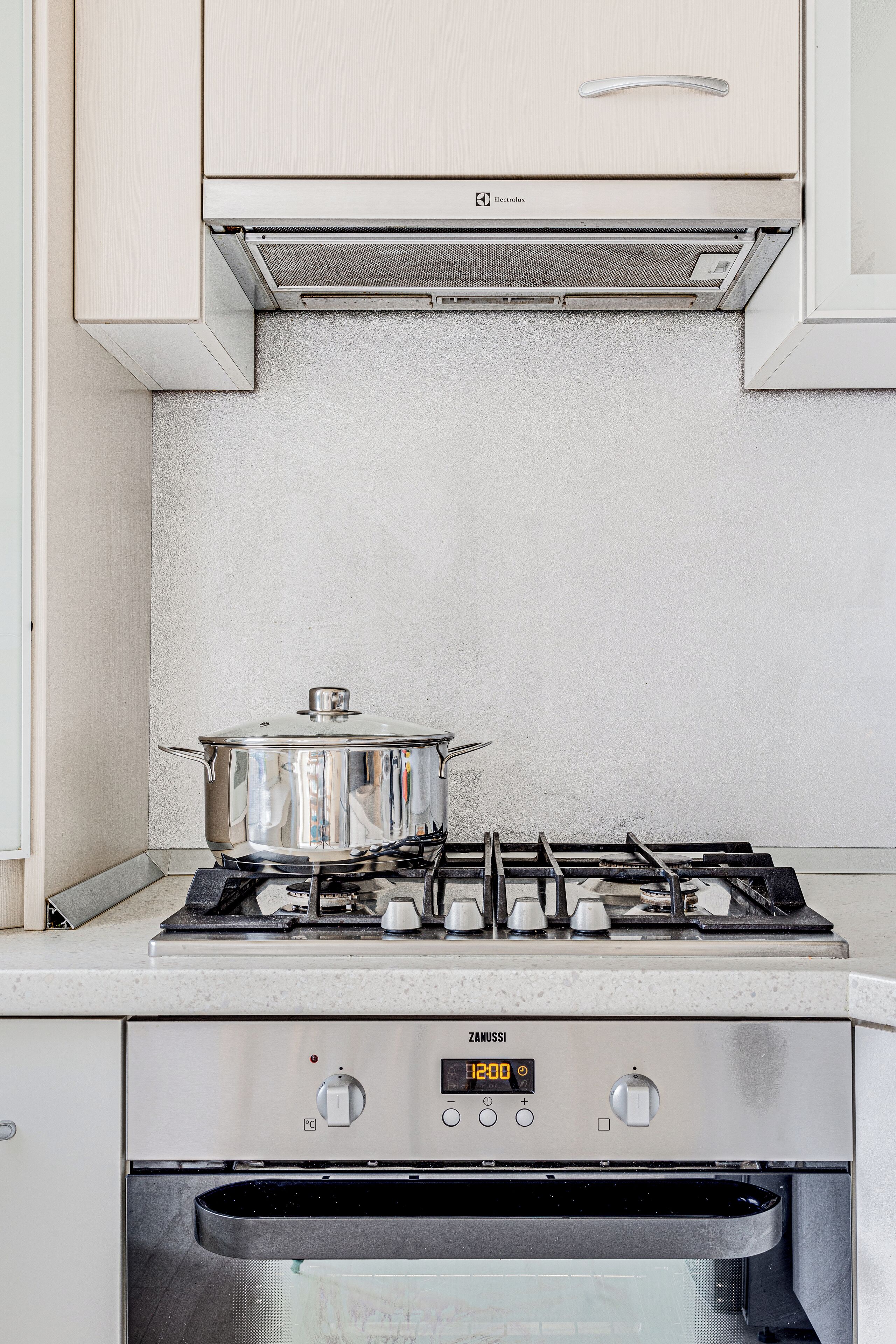 Una cocina con estufa a gas, una olla sobre la hornilla y un reloj digital que muestra las 12:00.