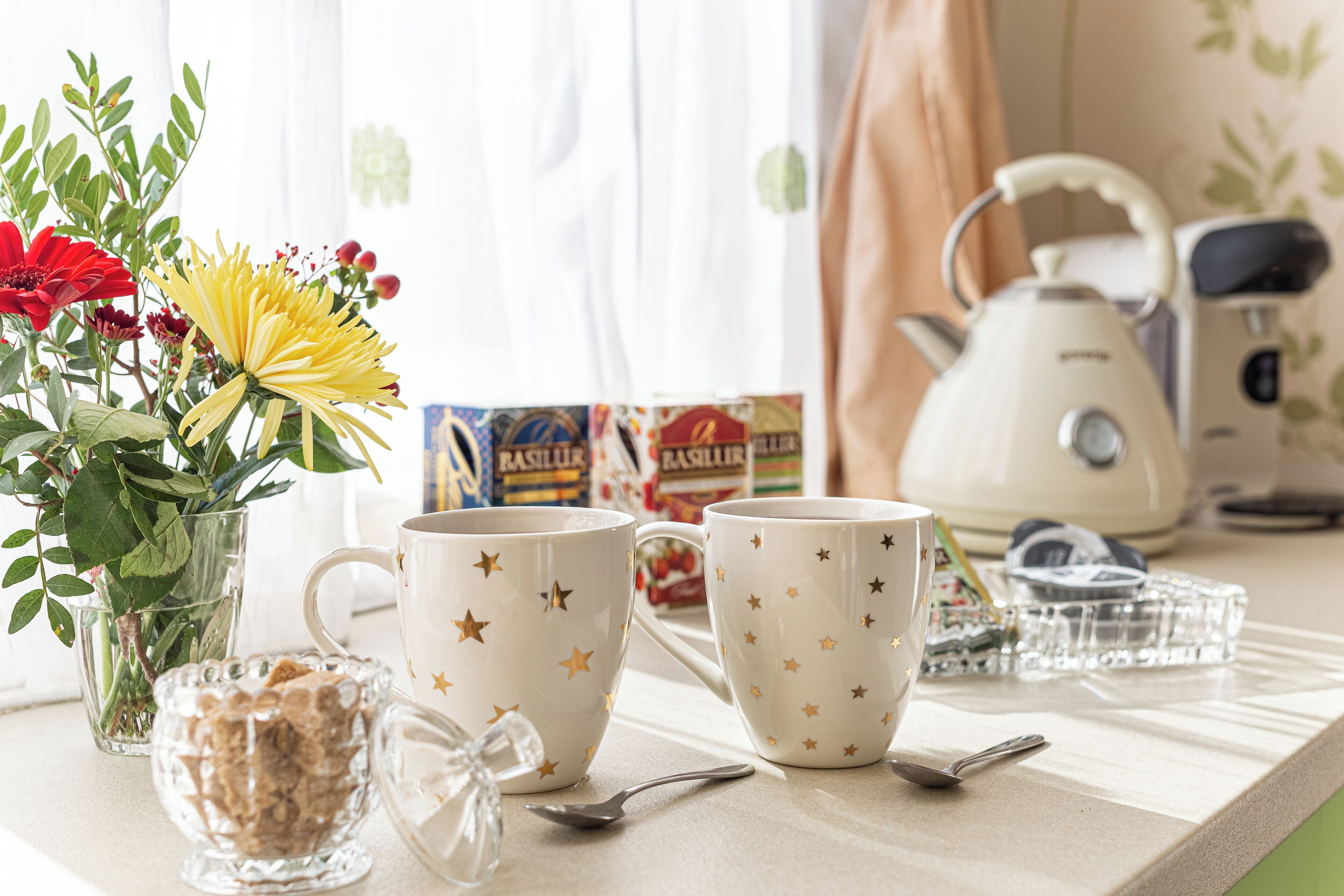 Un taulell de cuina amb dues tasses amb dibuixos de fulles, un got de cereals, una cullera i una tetera.