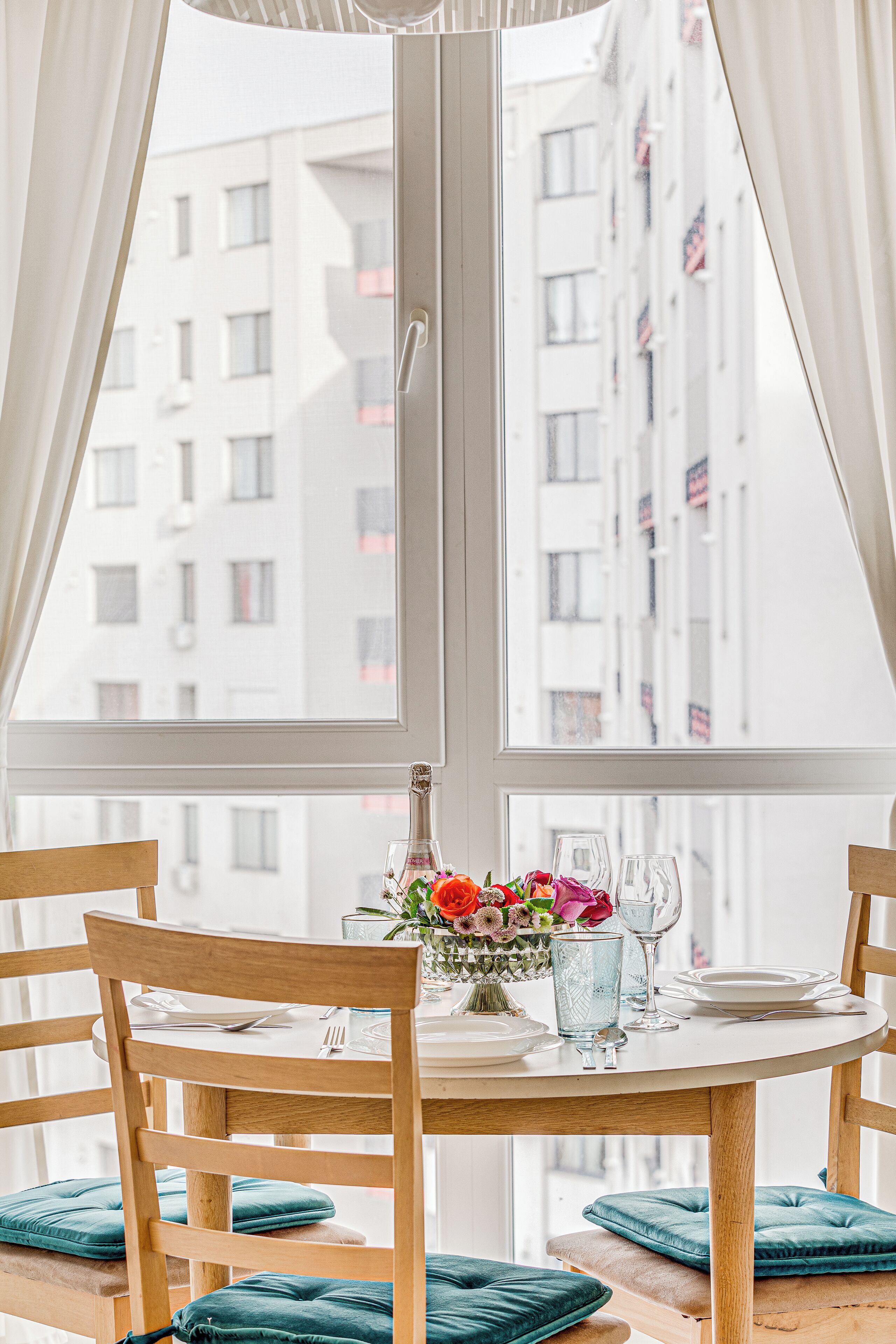 A dining table with chairs and a window view of a building with balconies.