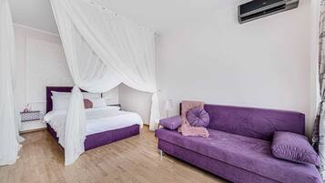 A bedroom with a canopy bed, a purple sofa, and a bedside table with a lamp.