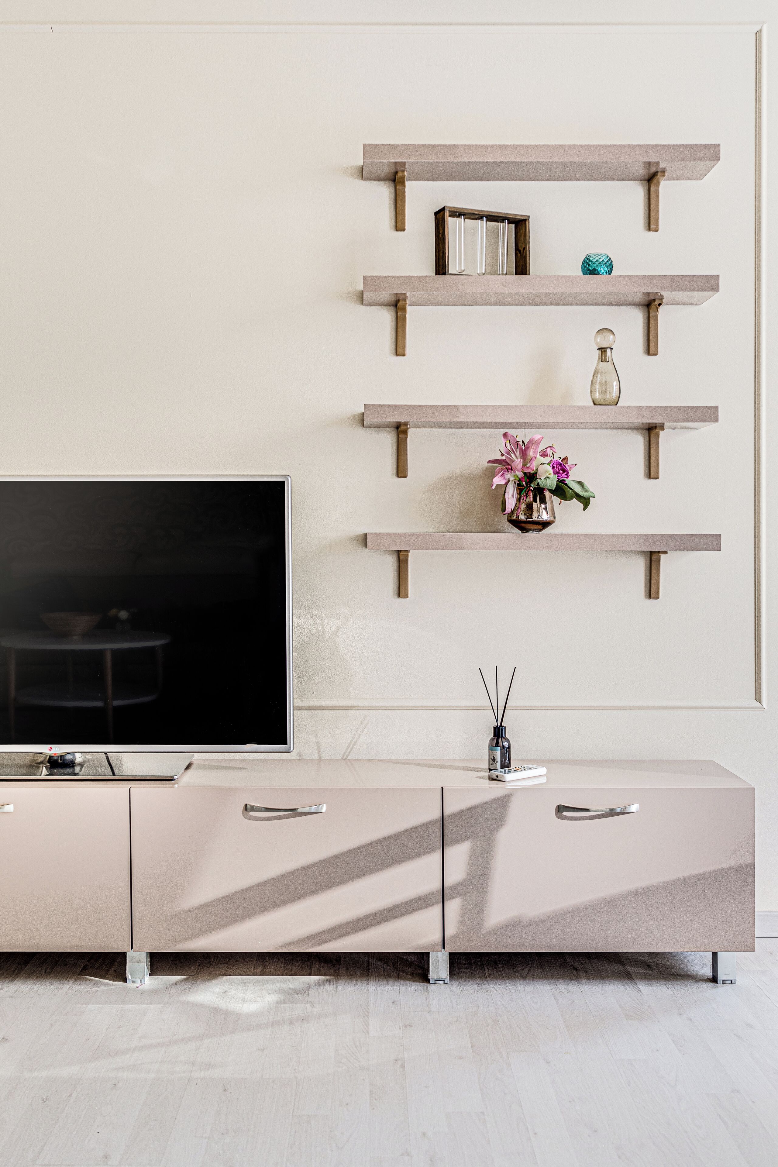 Una sala de estar moderna con un televisor de pantalla plana, un mueble color beige y estantes de madera con adornos.