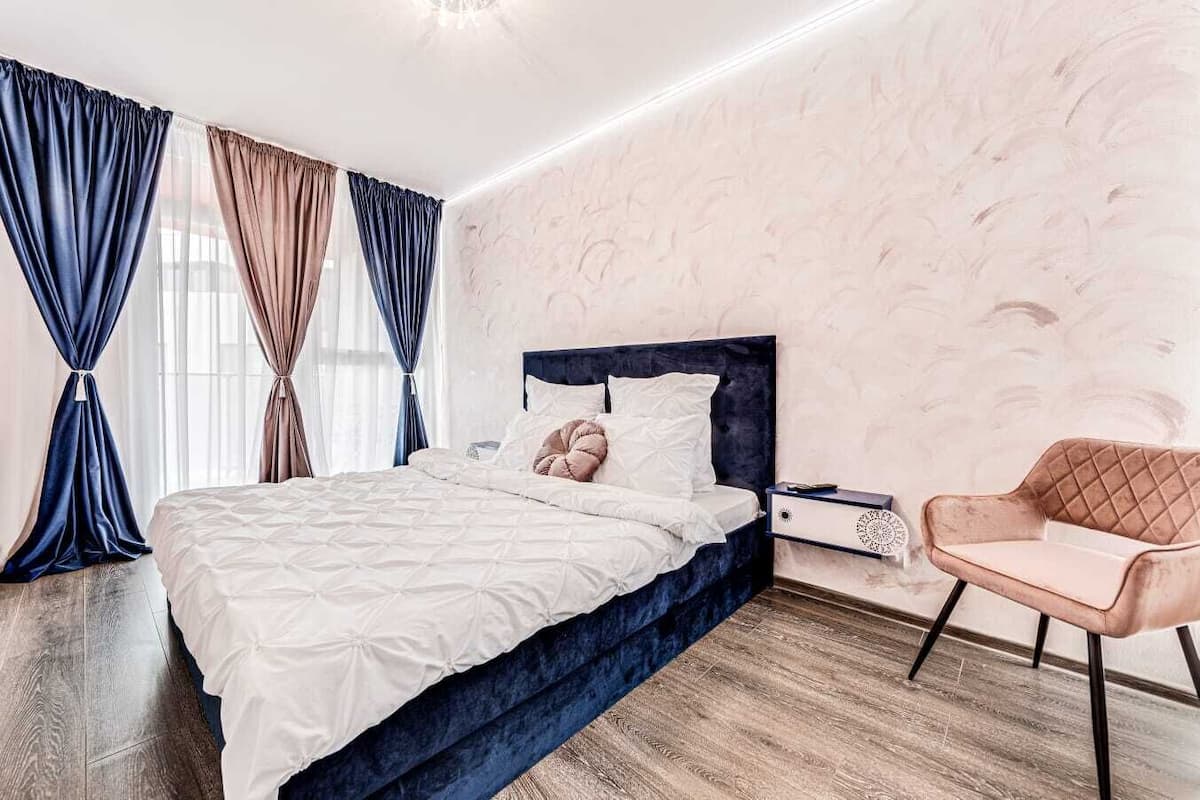 Ein modernes Schlafzimmer mit einem großen Bett, einem Nachttisch, einem Sessel und einer Wand mit Marmoroptik.