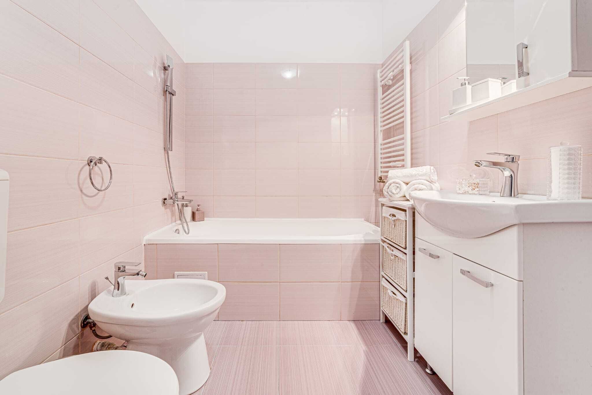 A modern bathroom with a bathtub, toilet, bidet, and a vanity with a mirror and shelves.