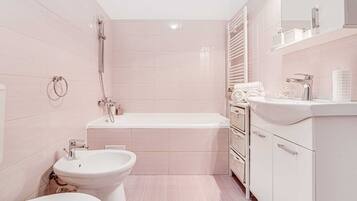 Ein modernes Badezimmer mit Badewanne, Toilette, Bidet und einem Waschtisch mit Spiegel und Ablageflächen.