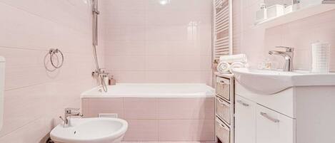 A modern bathroom with a bathtub, toilet, bidet, and a vanity with a mirror and shelves.