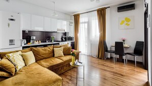A modern living room with a sofa, a dining table with chairs, and a kitchen in the background. - ARI - ARED Luxurious Apartments (Arad)