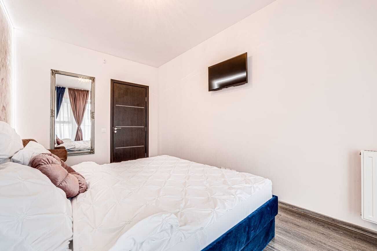 A bedroom with a bed, a television mounted on the wall, a door, and a window with curtains.