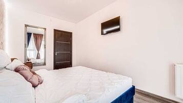 A bedroom with a bed, a television mounted on the wall, a door, and a window with curtains.