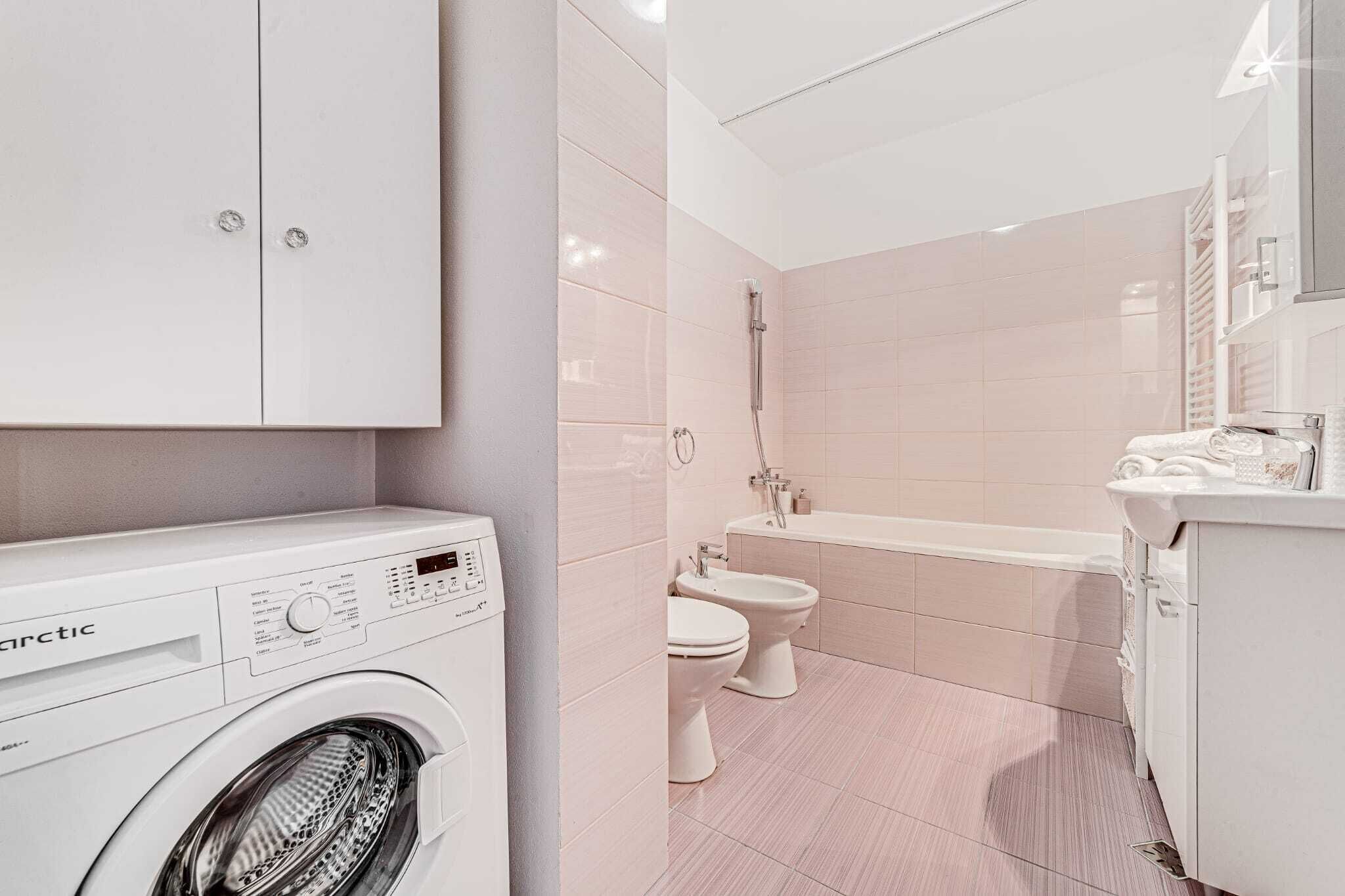 A modern bathroom with a washing machine, bidet, and bathtub.