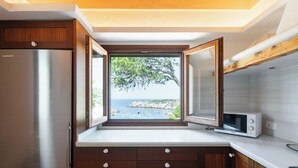 Una cocina con vista al mar, un refrigerador de acero inoxidable, armarios de madera y una encimera blanca.