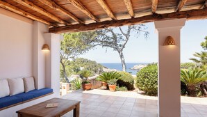 Un patio cubierto con un banco de madera y una mesa, con vistas a un paisaje pintoresco con árboles y el mar.