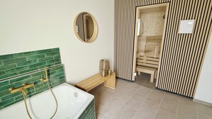 Une salle de bain avec une douche aux carreaux verts, une baignoire blanche, un banc en bois et un panneau mural en bois.