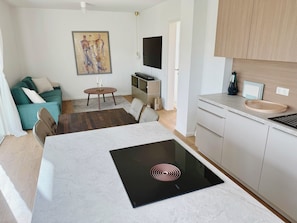 Uma cozinha moderna com um fogão por indução embutido, uma área de refeições com mesa e cadeiras, um sofá e um quadro na parede.