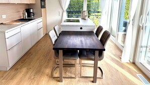 Une cuisine moderne avec un coin repas, des meubles en bois, un four encastré et une vue sur la verdure par la fenêtre.