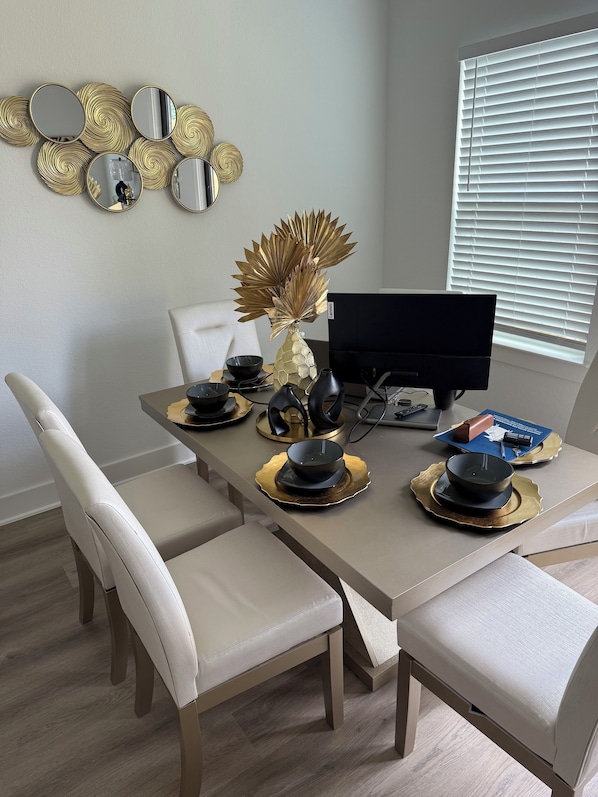 A dining area with a table set for four, featuring a modern design with gold and black accents, a vase with golden leaves, and a black monitor on the table.