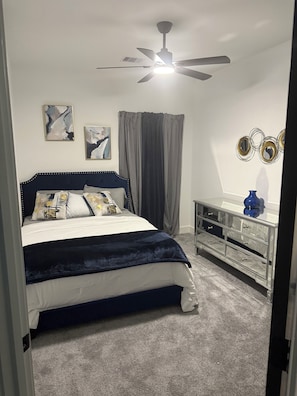 A bedroom with a bed, a ceiling fan, a dresser, and two wall-mounted mirrors.
