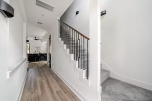 Un interior moderno con suelo de madera, paredes blancas y una escalera con barandillas negras.