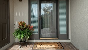 Puerta principal con un tapete de 'Bienvenido', una planta en maceta y un buzón.