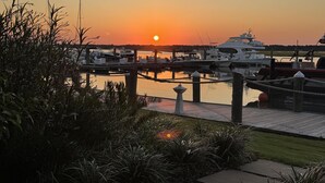 Un puerto deportivo al atardecer con barcos amarrados, un paseo marítimo de madera y una zona verde.