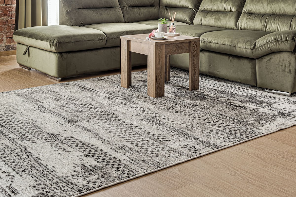 Un salon avec un canapé d’angle vert, un tapis à motifs, une table basse en bois et un mur en briques.