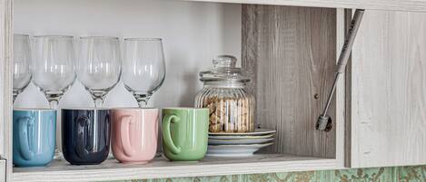 A kitchen cabinet with a handle, a shelf with clear glasses, and a glass jar with cookies.