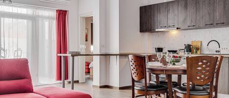 Una sala de estar moderna con un sofá rojo, un comedor con una mesa y sillas de madera, y una cocina con armarios de madera oscura.