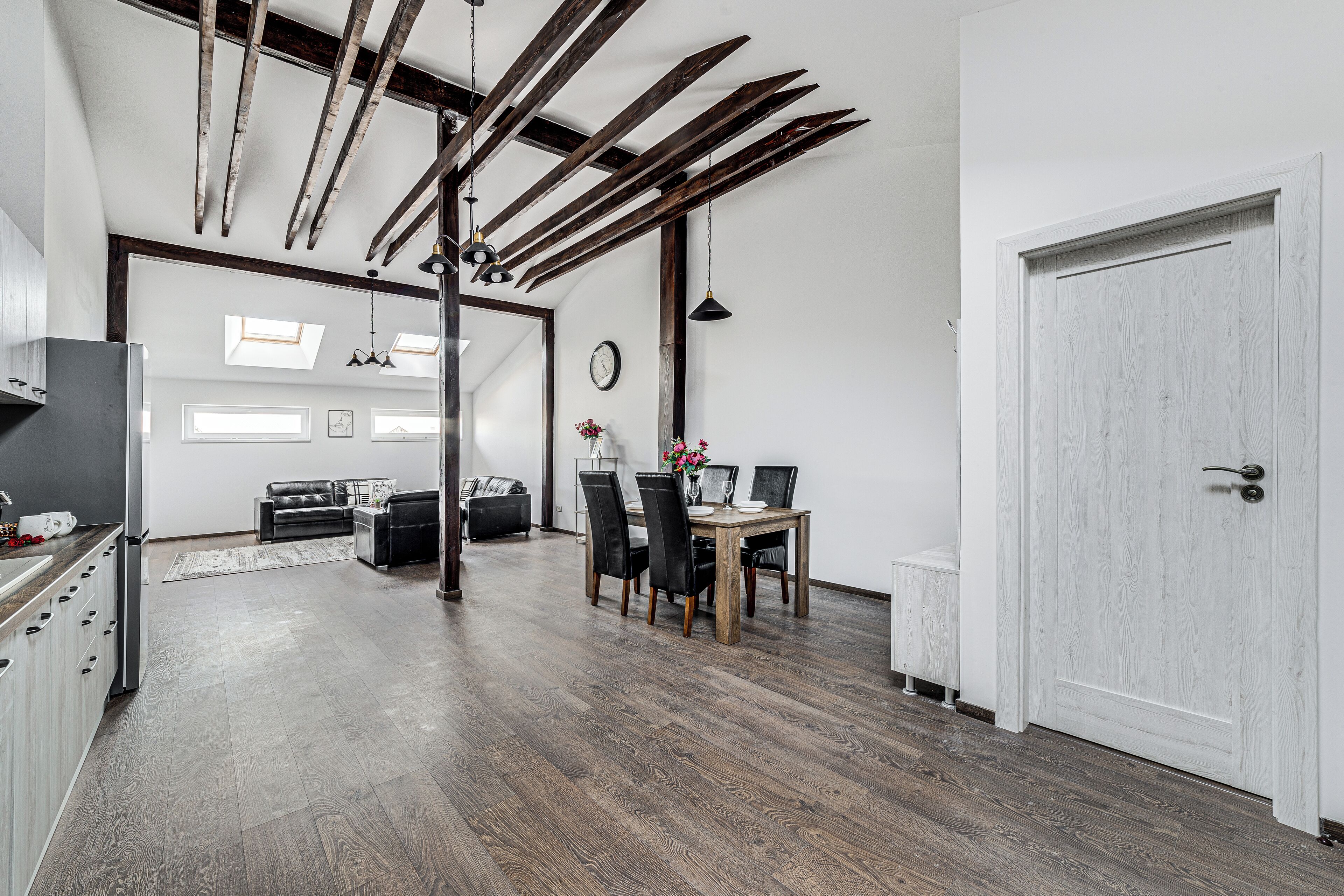 Una cocina moderna con suelo de madera, una zona de comedor con mesa y sillas, y una puerta blanca.