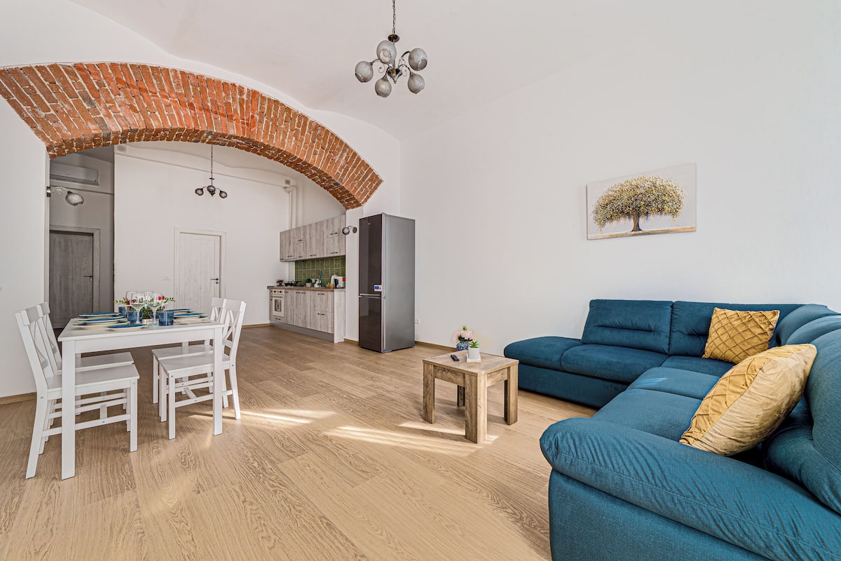 Un salon moderne avec un canapé bleu, une table à manger et des chaises, et un coin cuisine à l’arrière-plan.